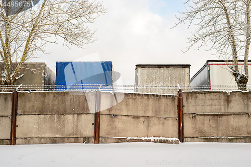 Image of Trucks standing behind the fence wall in winter.