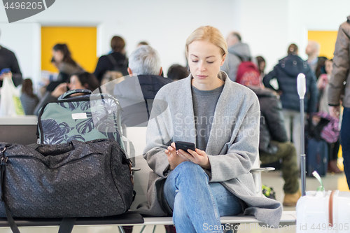 Image of Female traveler using her cell phone while waiting to board a plane at departure gates at airport terminal.