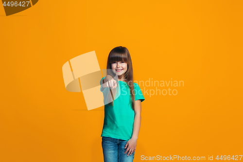 Image of The happy teen girl pointing to you, half length closeup portrait on orange background.