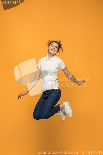 Image of Freedom in moving. Pretty young woman jumping against orange background