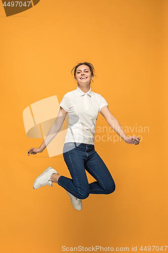 Image of Freedom in moving. Pretty young woman jumping against orange background