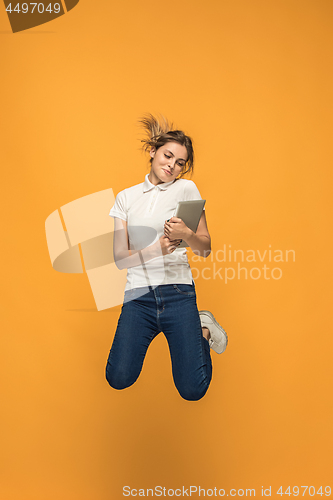 Image of Image of young woman over orange background using laptop computer or tablet gadget while jumping.