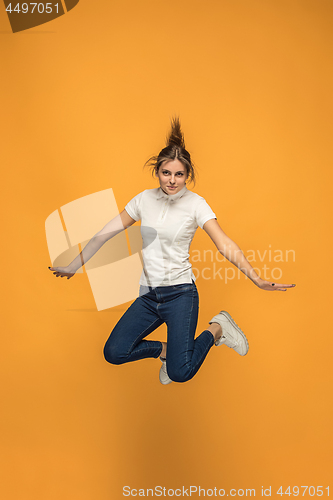 Image of Freedom in moving. Pretty young woman jumping against orange background