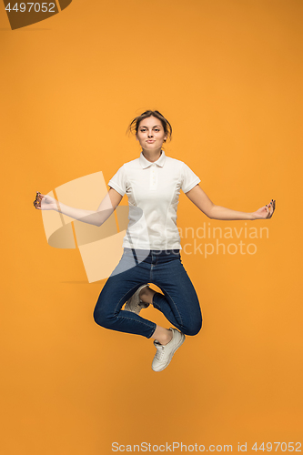 Image of Freedom in moving. Pretty young woman jumping against orange background