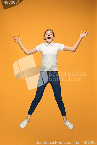 Image of Freedom in moving. Pretty young woman jumping against orange background