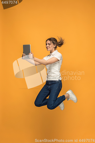 Image of Image of young woman over orange background using laptop computer or tablet gadget while jumping.