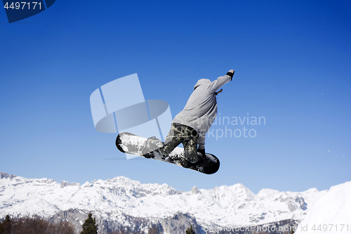 Image of Extreme Jumping Snowboarder at jump above mountains at sunny day