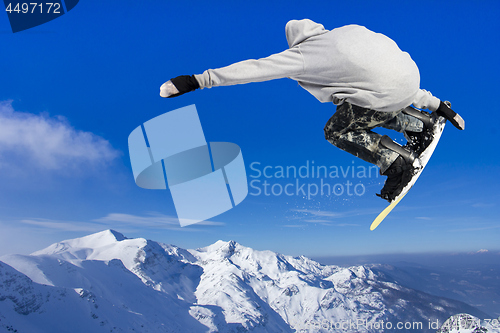 Image of Extreme Jumping Snowboarder at jump above mountains at sunny day