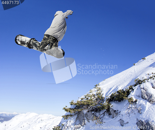 Image of Extreme Jumping Snowboarder at jump above mountains at sunny day