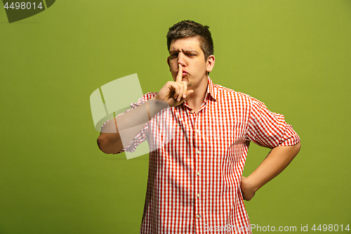 Image of The young man whispering a secret behind her hand over green background