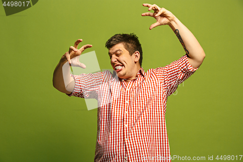 Image of The young emotional angry man screaming on green studio background