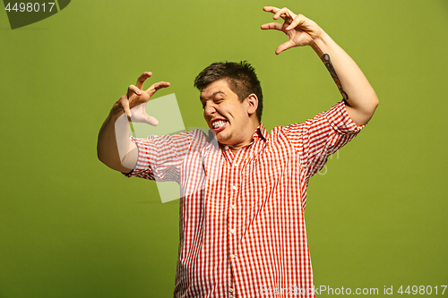 Image of The young emotional angry man screaming on green studio background