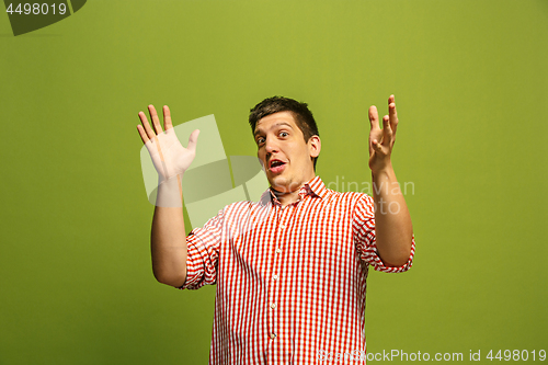 Image of The young attractive man looking suprised isolated on green