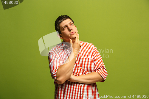 Image of Let me think. Doubtful pensive man with thoughtful expression making choice against green background