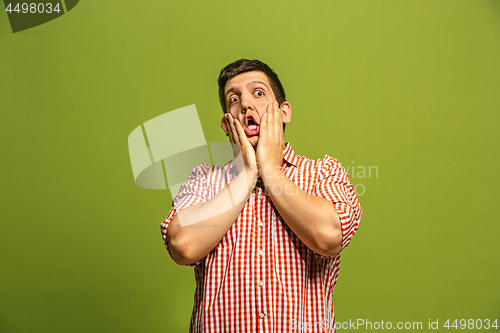Image of The young attractive man looking suprised isolated on green
