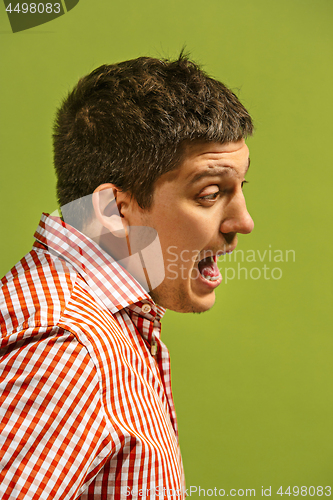 Image of The young emotional angry man screaming on green studio background