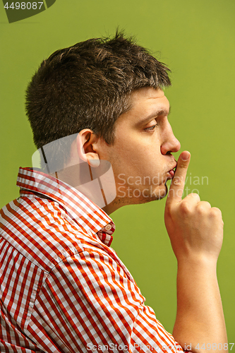 Image of The young man whispering a secret behind her hand over green background