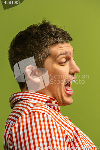 Image of The young emotional angry man screaming on green studio background