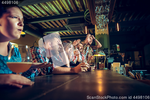 Image of Upset male and female friends watching sport game or football match and drinking beer at bar or pub.