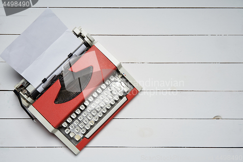 Image of red vintage typewriter with white blank paper sheet on white wooden table