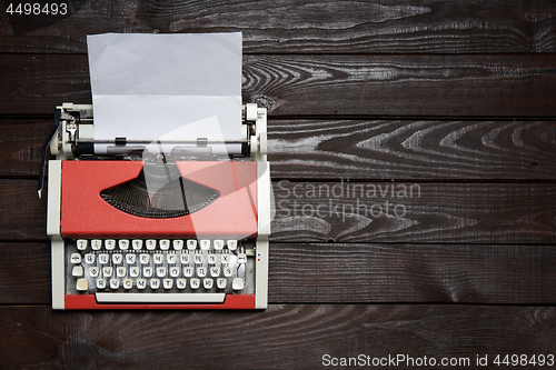 Image of red vintage typewriter with white blank paper sheet on dark wooden table