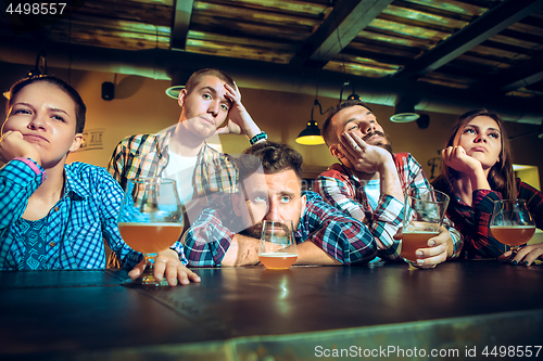 Image of Upset male and female friends watching sport game or football match and drinking beer at bar or pub.