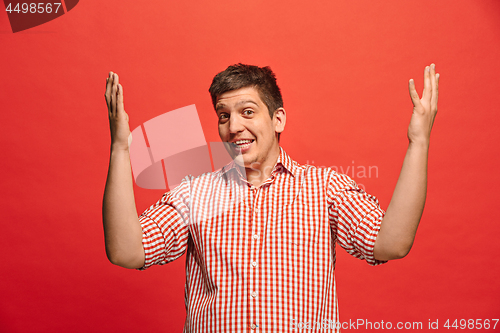 Image of The young attractive man looking suprised isolated on red