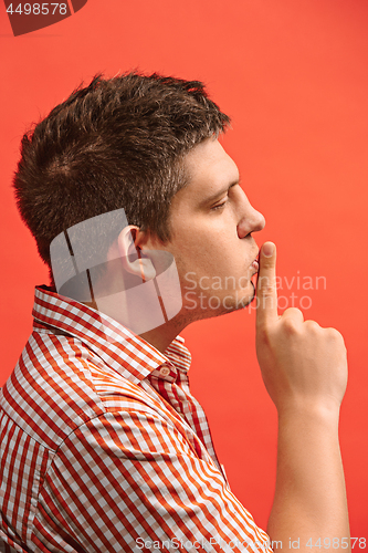 Image of The young man whispering a secret behind her hand over red background