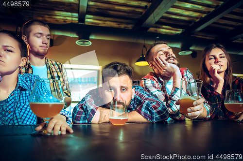 Image of Upset male and female friends watching sport game or football match and drinking beer at bar or pub.