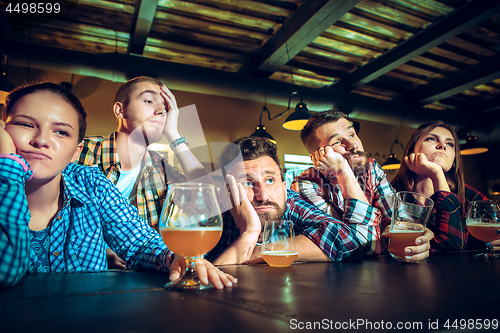 Image of Upset male and female friends watching sport game or football match and drinking beer at bar or pub.