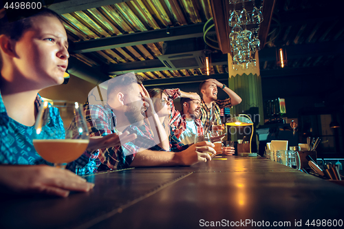 Image of Upset male and female friends watching sport game or football match and drinking beer at bar or pub.