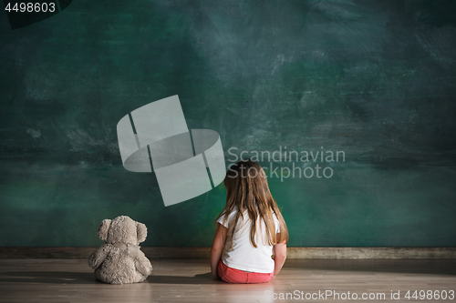 Image of Little girl with teddy bear sitting on floor in empty room. Autism concept