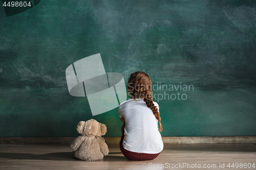 Image of Little girl with teddy bear sitting on floor in empty room. Autism concept