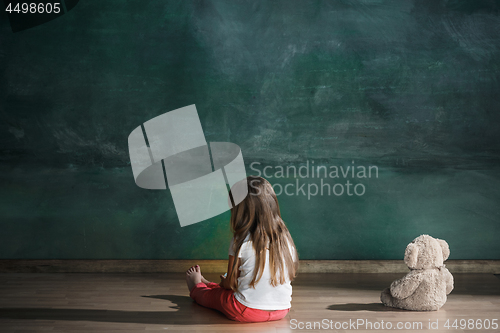 Image of Little girl with teddy bear sitting on floor in empty room. Autism concept