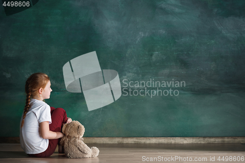 Image of Little girl with teddy bear sitting on floor in empty room. Autism concept