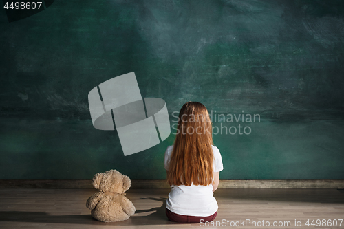 Image of Little girl with teddy bear sitting on floor in empty room. Autism concept