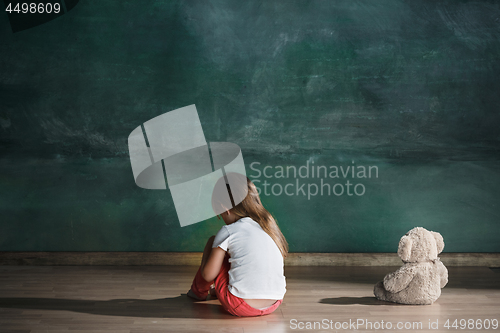 Image of Little girl with teddy bear sitting on floor in empty room. Autism concept