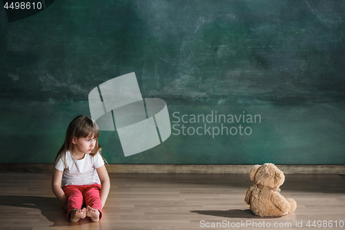 Image of Little girl with teddy bear sitting on floor in empty room. Autism concept