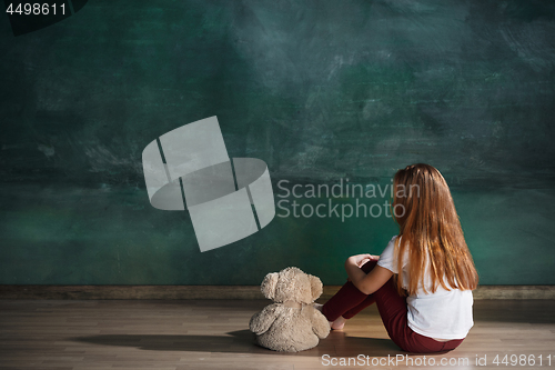 Image of Little girl with teddy bear sitting on floor in empty room. Autism concept