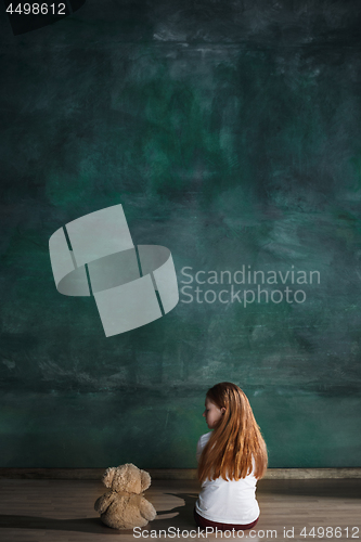 Image of Little girl with teddy bear sitting on floor in empty room. Autism concept