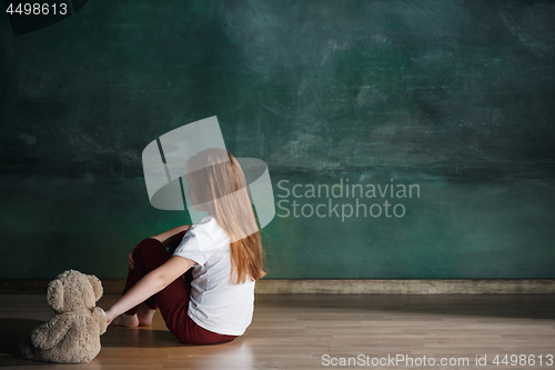 Image of Little girl with teddy bear sitting on floor in empty room. Autism concept