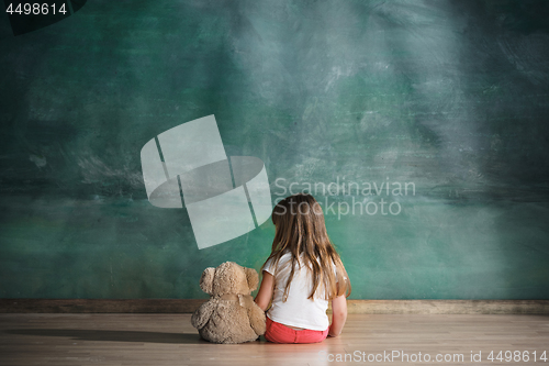 Image of Little girl with teddy bear sitting on floor in empty room. Autism concept