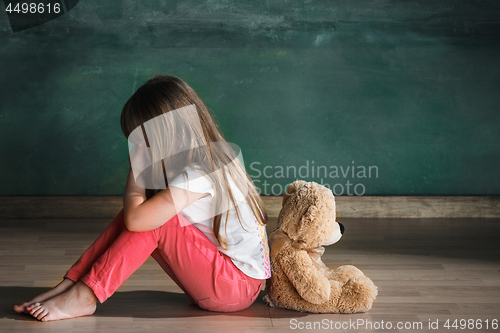 Image of Little girl with teddy bear sitting on floor in empty room. Autism concept