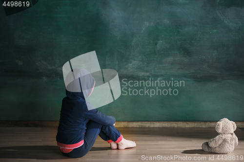 Image of Little girl with teddy bear sitting on floor in empty room. Autism concept