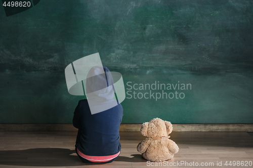 Image of Little girl with teddy bear sitting on floor in empty room. Autism concept