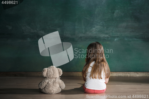 Image of Little girl with teddy bear sitting on floor in empty room. Autism concept