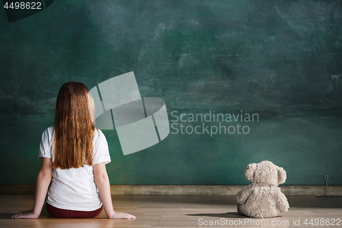 Image of Little girl with teddy bear sitting on floor in empty room. Autism concept