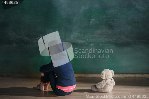 Image of Little girl with teddy bear sitting on floor in empty room. Autism concept