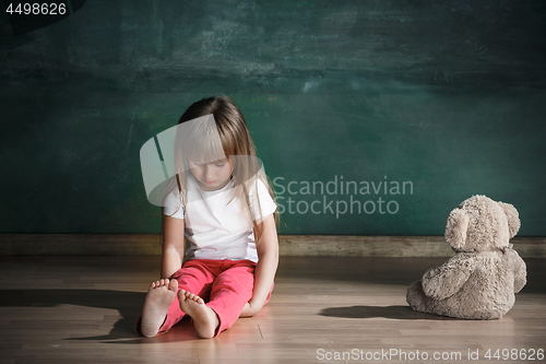 Image of Little girl with teddy bear sitting on floor in empty room. Autism concept