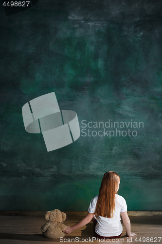 Image of Little girl with teddy bear sitting on floor in empty room. Autism concept